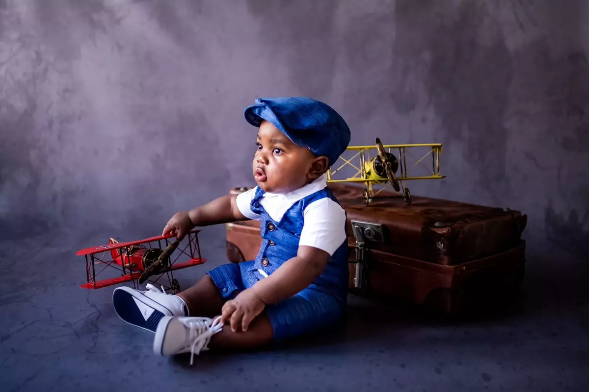 Baby boy dressed as an aviator with toy airplanes and a vintage suitcase