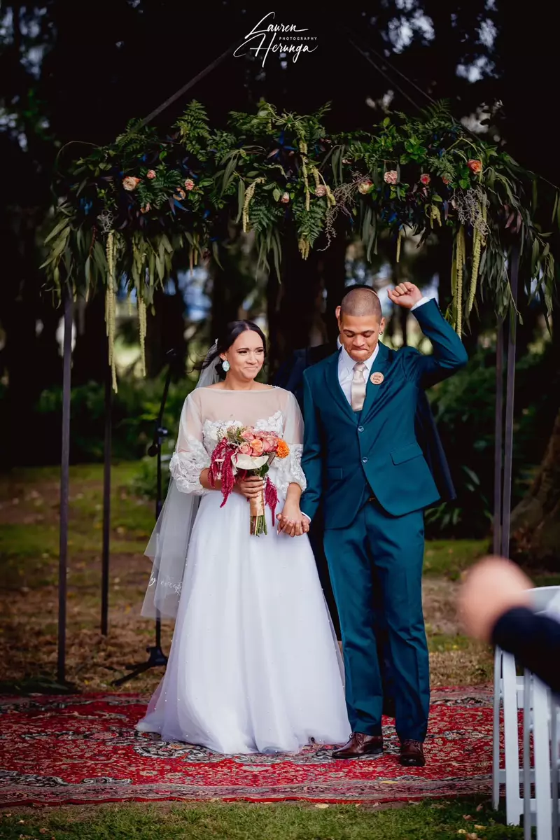 A newlywed couple at an outdoor wedding ceremony under a floral archway