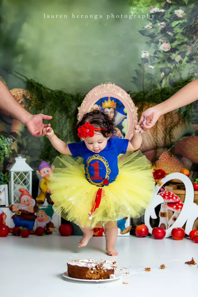 A one-year-old baby girl dressed as Snow White above a partially eaten cake