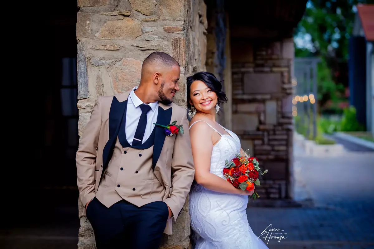Bride and groom leaning against stone pillar outdoors