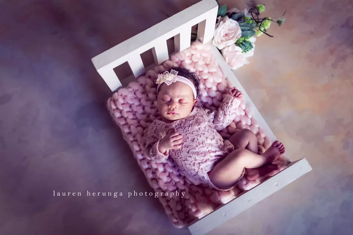 Newborn baby sleeping in a small white wooden bed with pink bedding and floral decorations