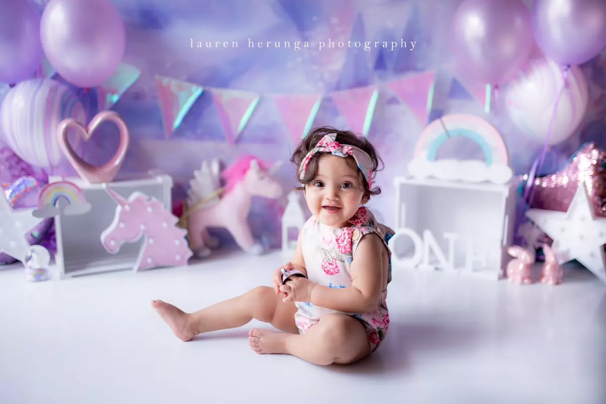 Baby girl sitting in a fantasy unicorn-themed birthday setup with balloons and decorations