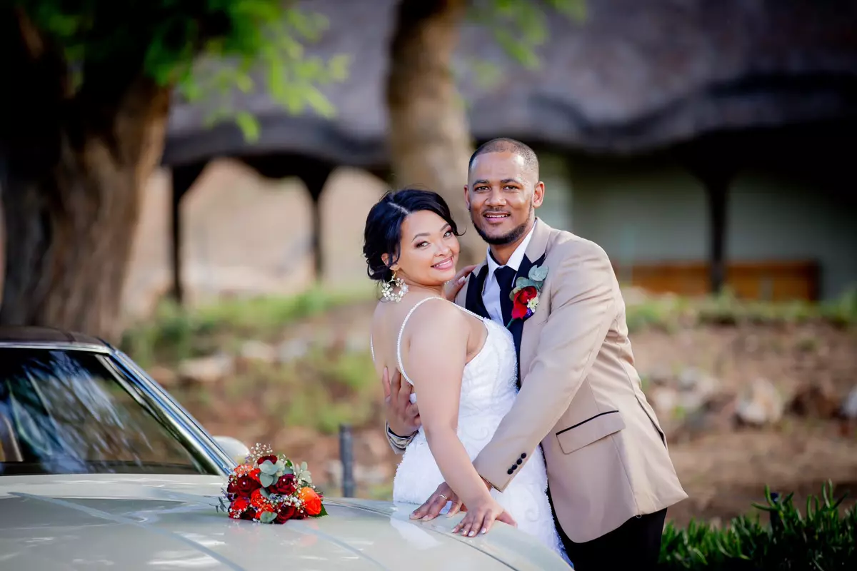 Bride and groom posing outdoors by a car