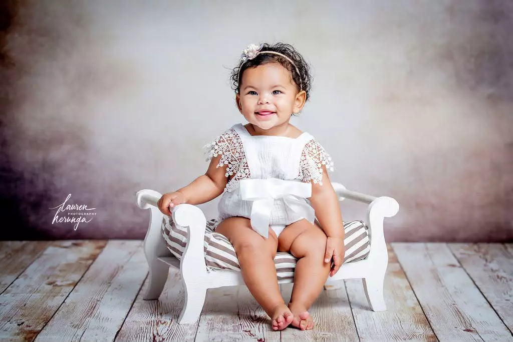 Baby girl sitting on a miniature white wooden bed