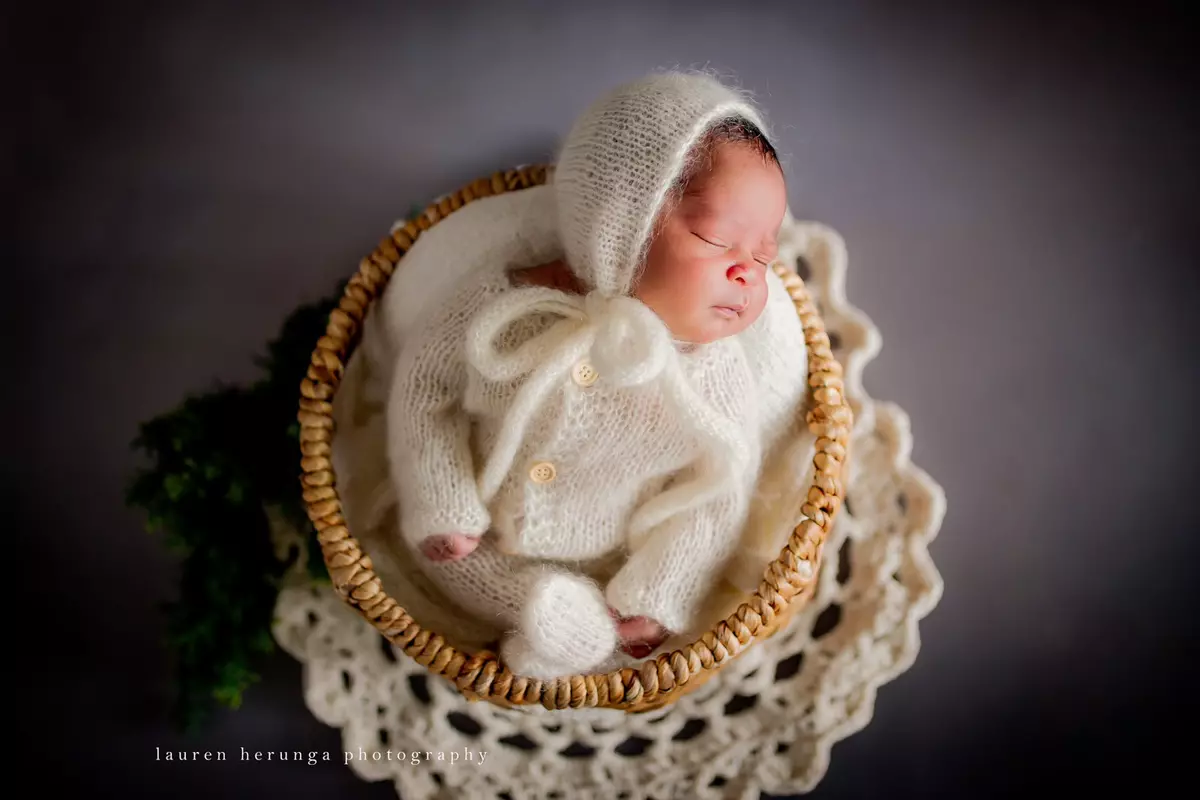 Sleeping newborn baby in a knitted outfit and bonnet, nestled in a wicker basket
