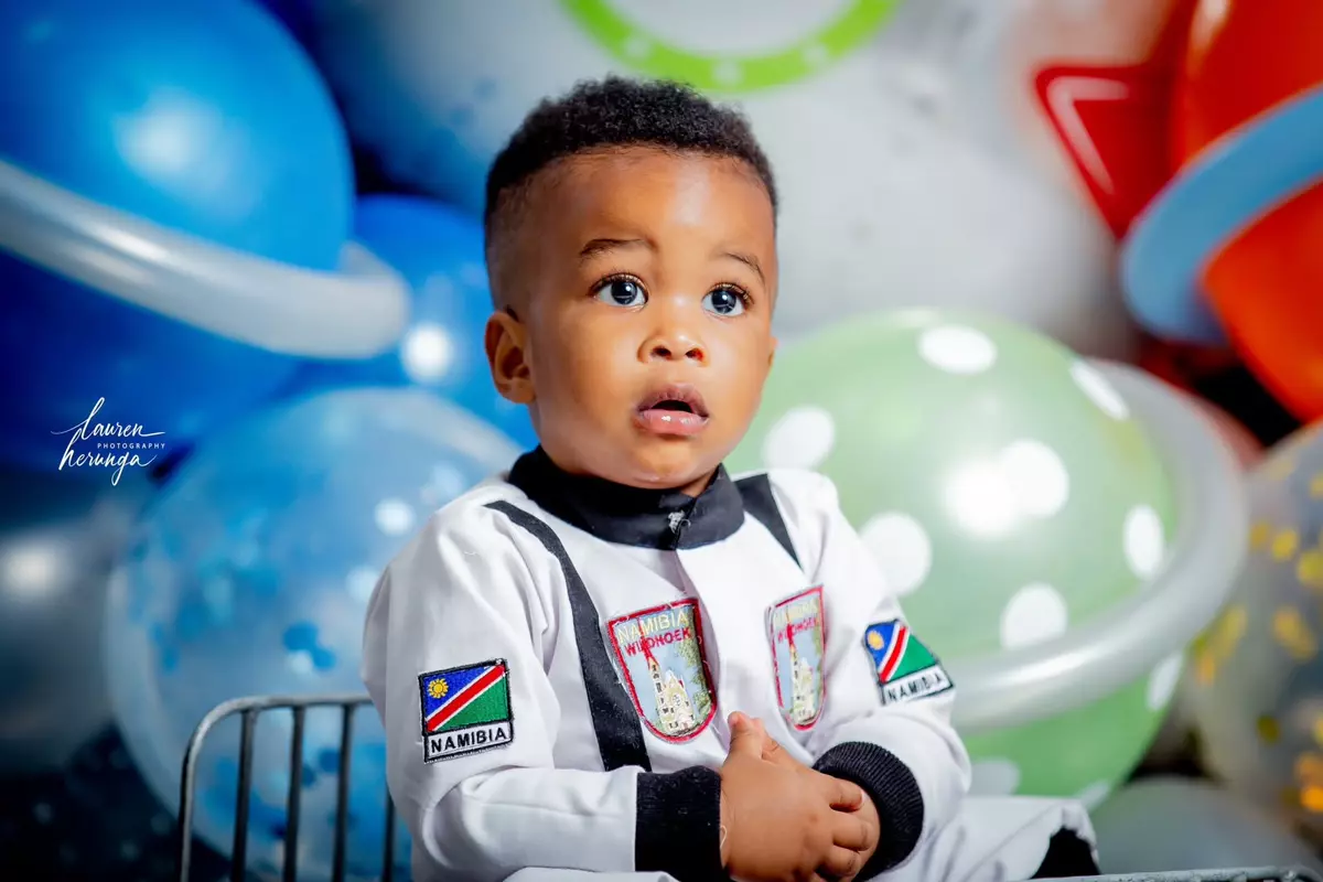 A toddler dressed as an astronaut sitting in front of a balloon display