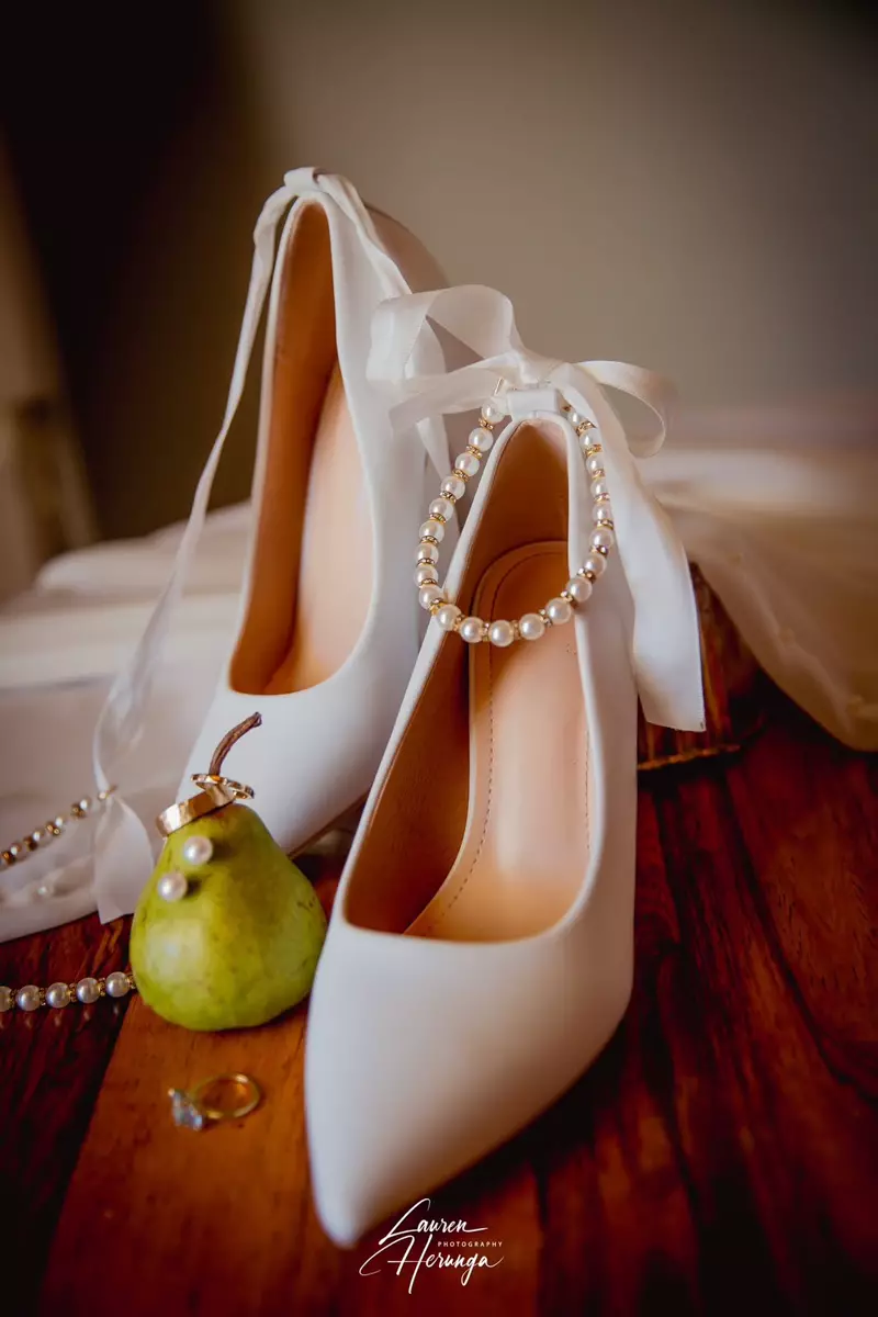 Bridal shoes, rings, and pear on a wooden surface