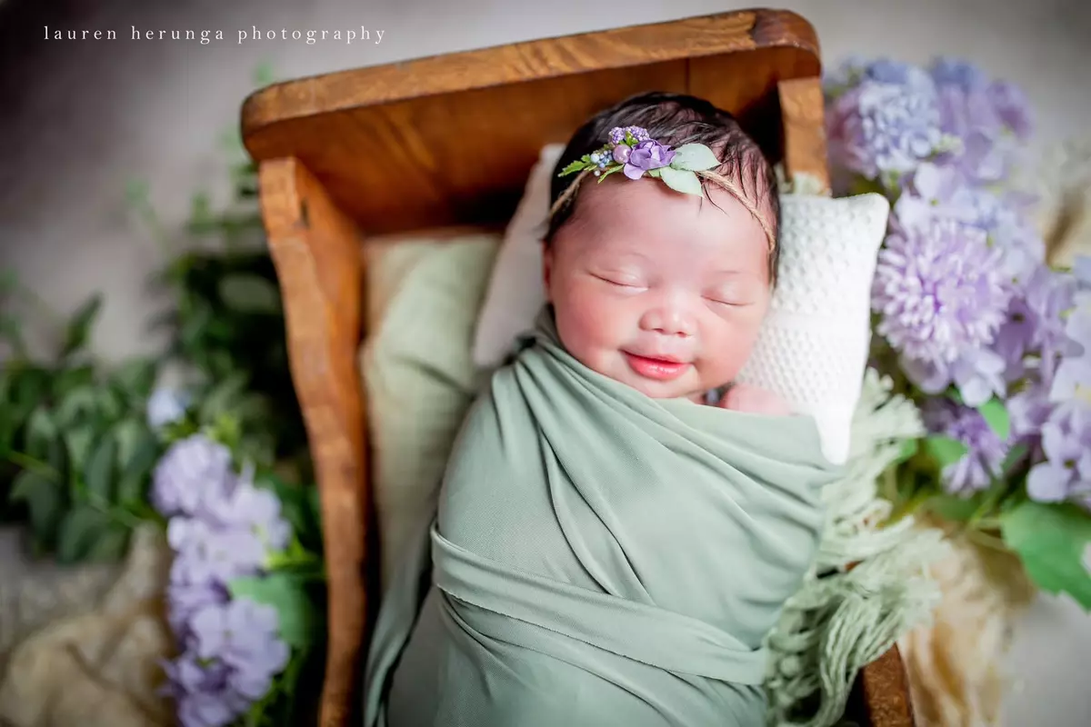 Newborn baby smiling in wooden prop bed