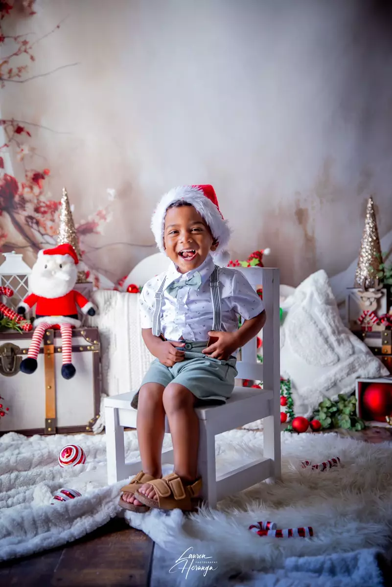 A smiling young boy in a Christmas outfit seated on a white chair