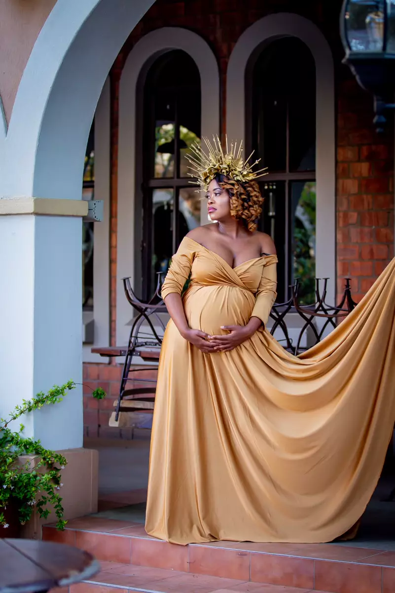 Pregnant woman in a gold dress and crown standing outdoors