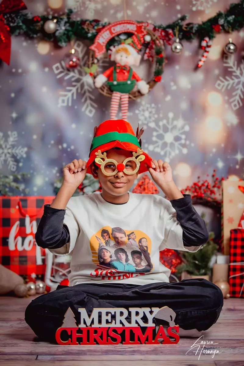 Boy wearing a Christmas hat and glasses sitting in front of a Christmas backdrop