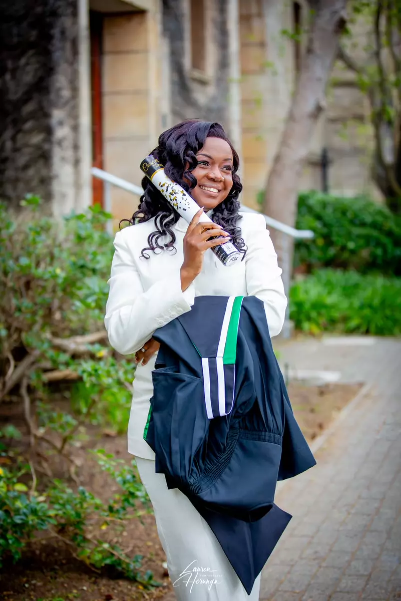 Graduation celebration portrait of a smiling woman in a white suit holding a confetti cannon