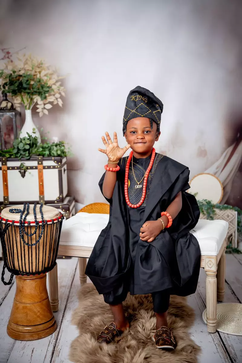 A young boy in traditional black attire and a matching cap, adorned with coral beads