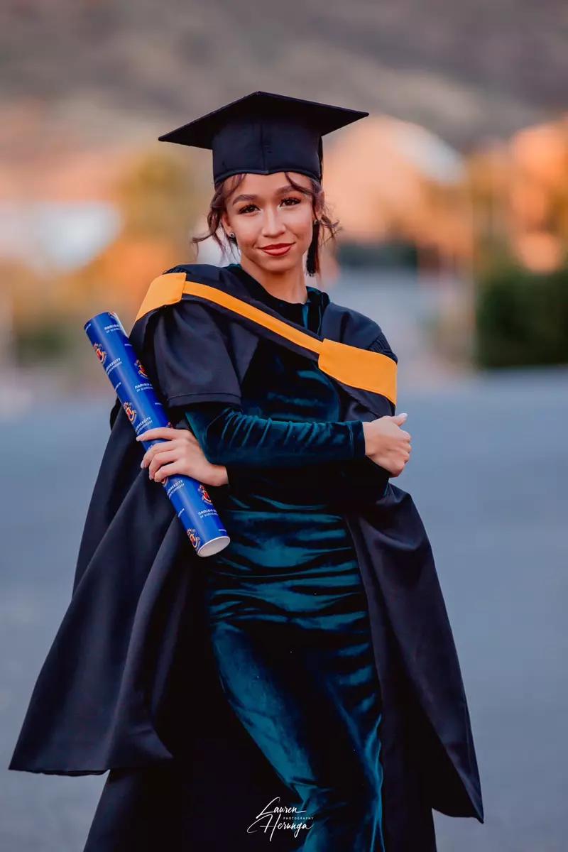 A young woman in graduation gown, cap, and holding a scroll