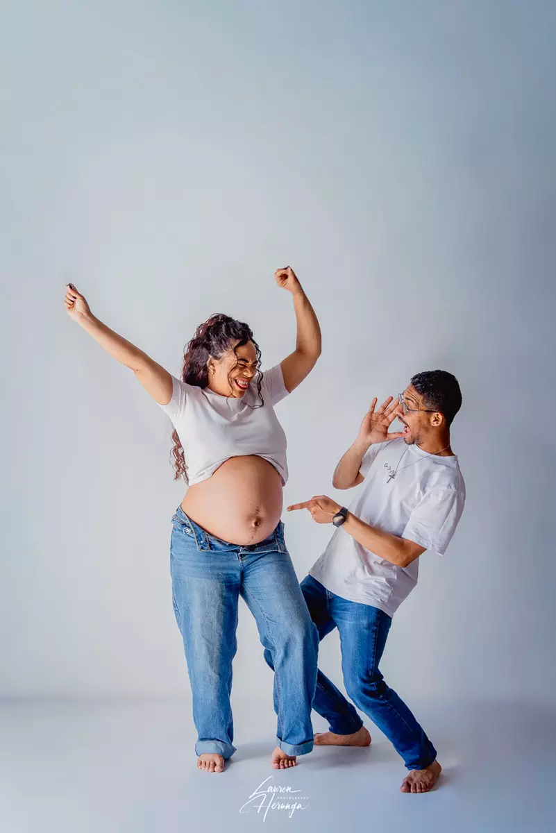 Expectant parents posing playfully in a studio