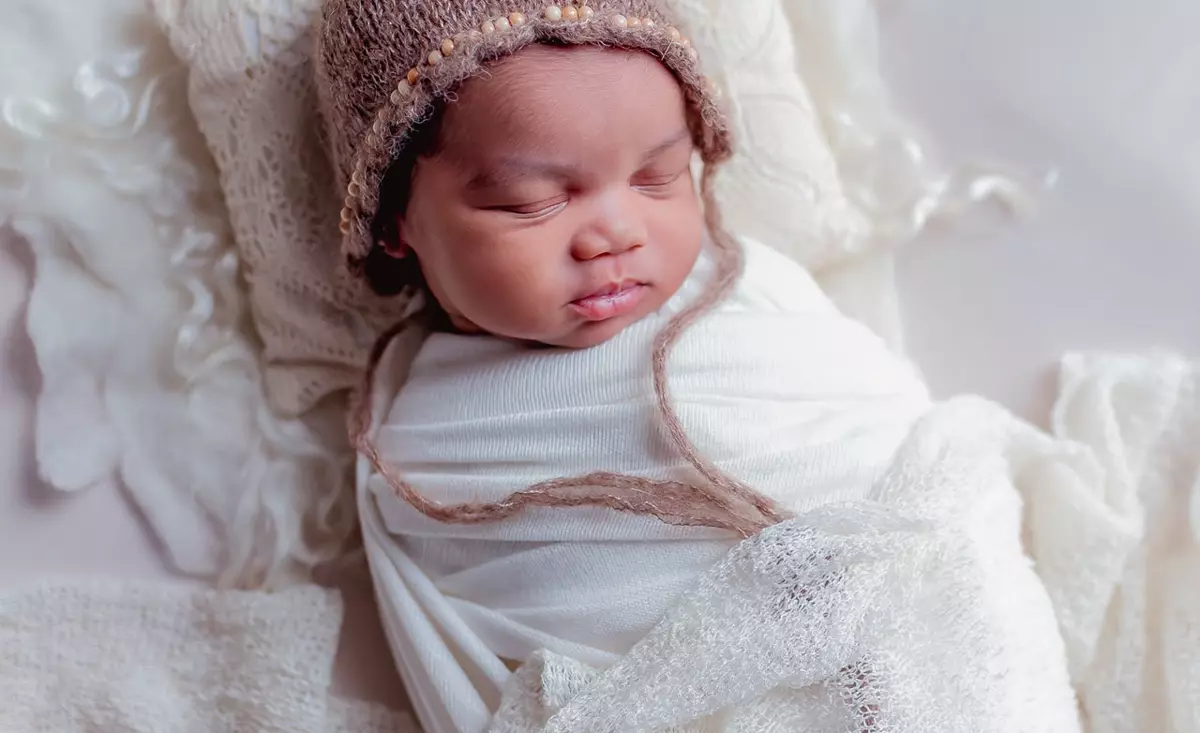 Sleeping newborn baby wrapped in white swaddle and wearing a brown knitted bonnet