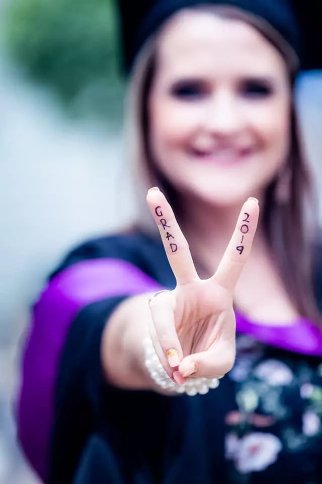 A smiling graduate holding up fingers with GRAD 2019 written on them