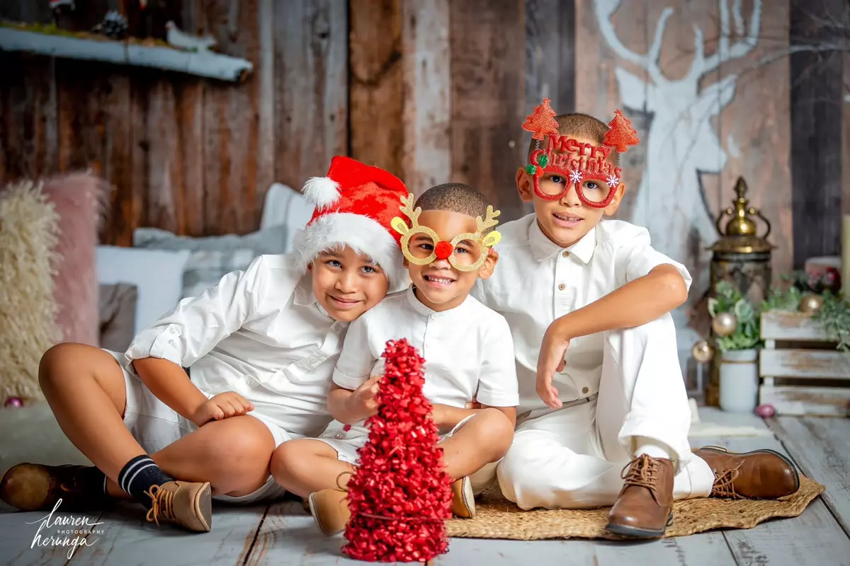 Three young boys dressed in white shirts and Christmas accessories
