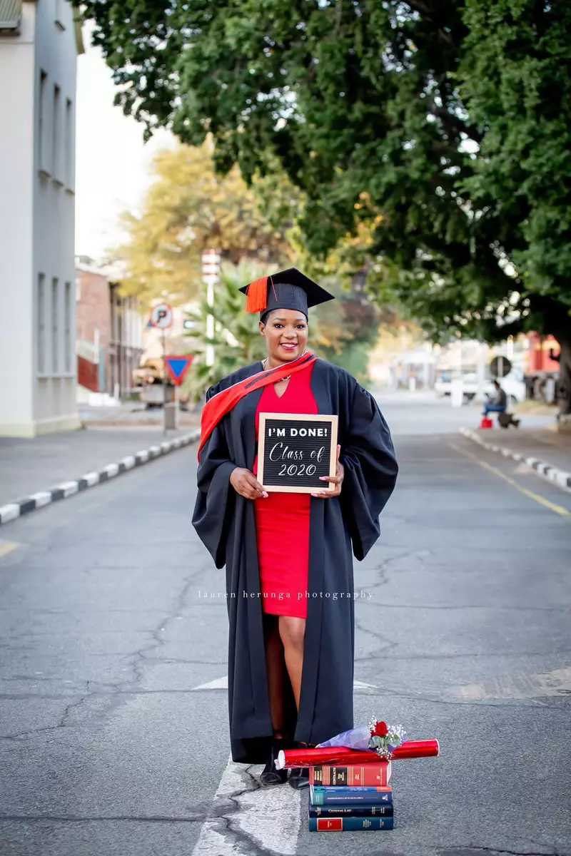 A graduate in a cap and gown holding a sign