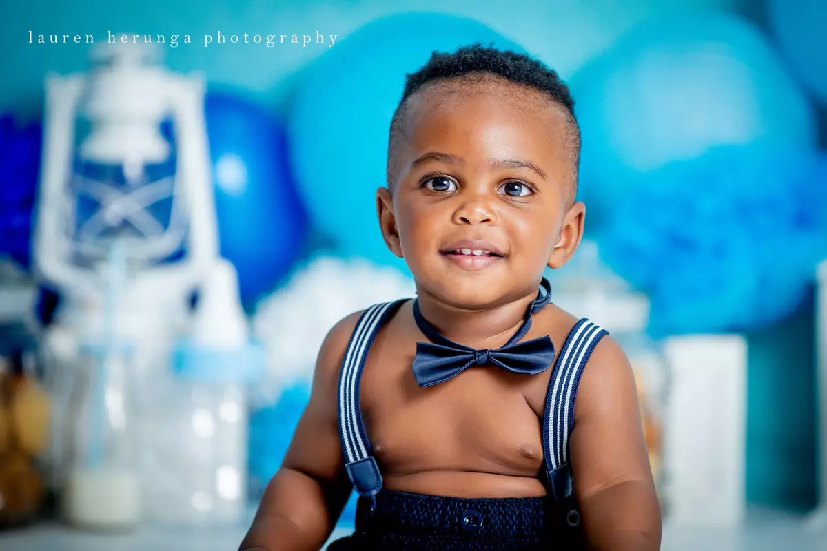 A smiling young boy with dark hair wearing blue suspenders and a bow tie