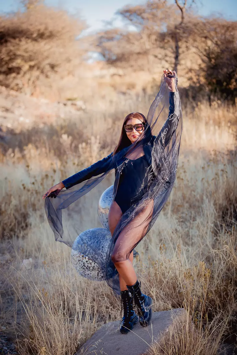 Woman in black outfit posing outdoors in a grassy landscape