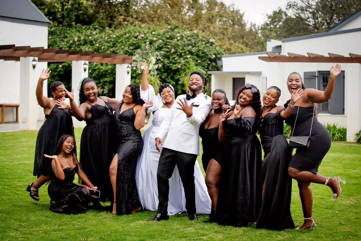 A wedding party posing on a lawn outside buildings with white walls and pergolas