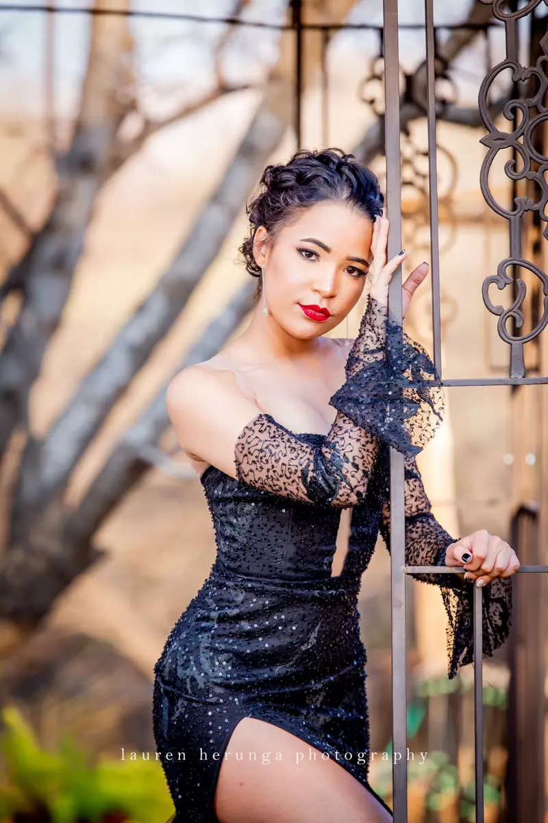Young woman in black dress leaning against a metal structure