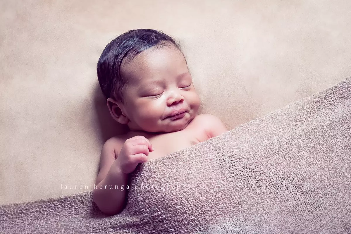 Sleeping newborn baby wrapped in a pink knitted blanket on a neutral background