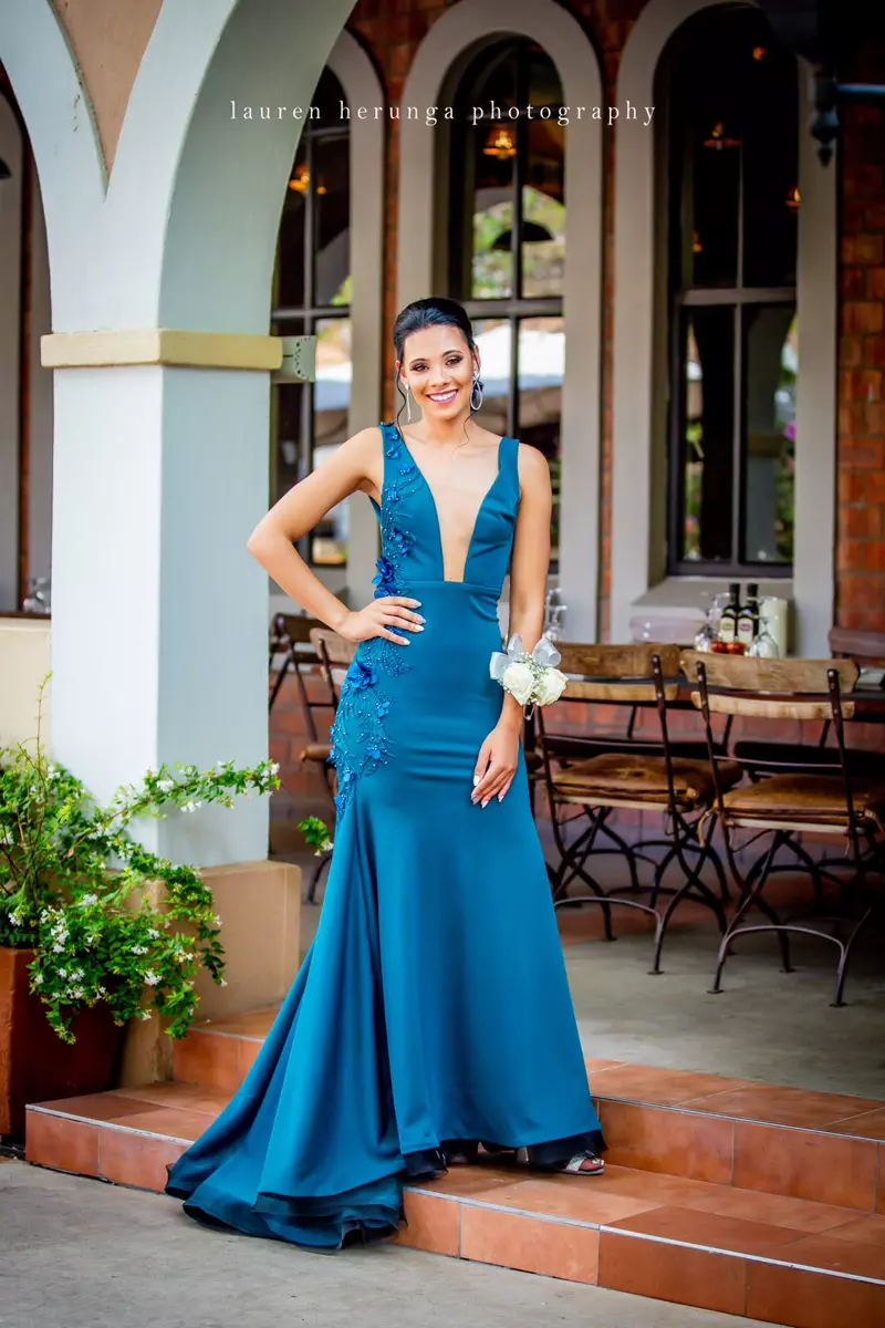 A young woman wearing a long teal evening gown standing on outdoor steps
