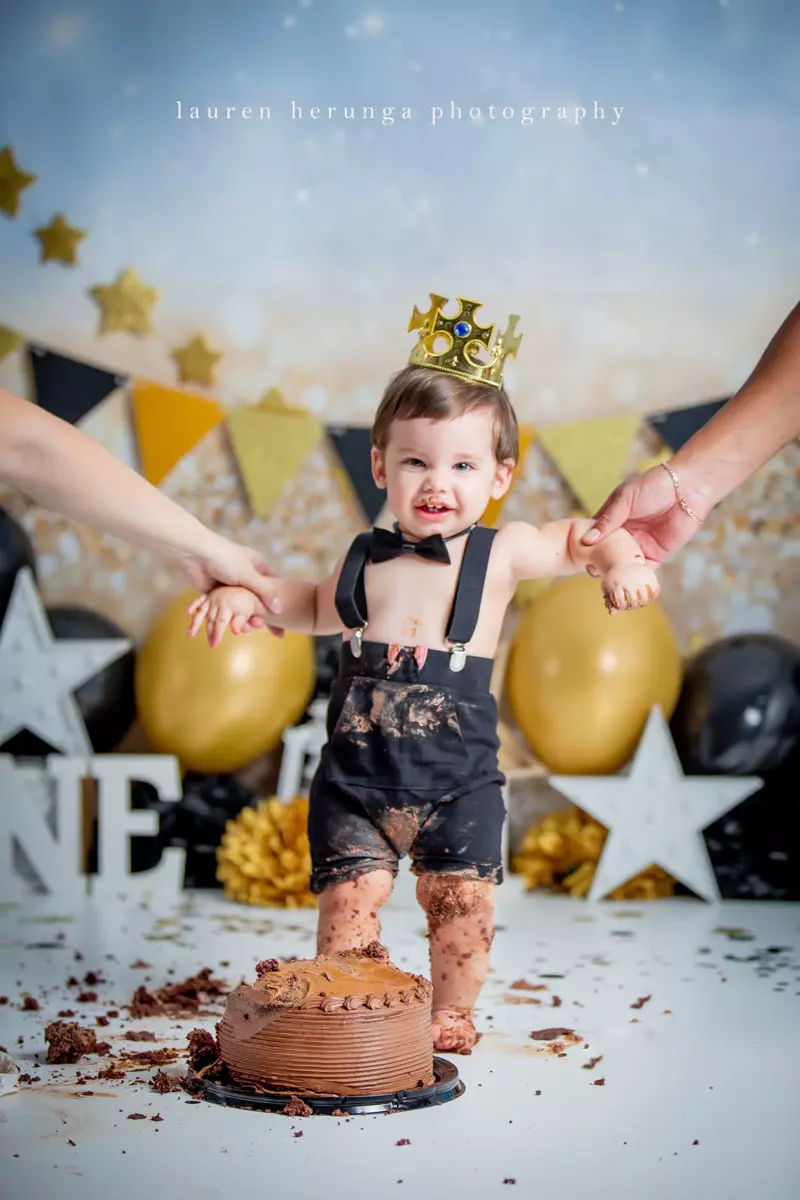 Baby boy standing in front of a smash cake wearing a crown and suspenders