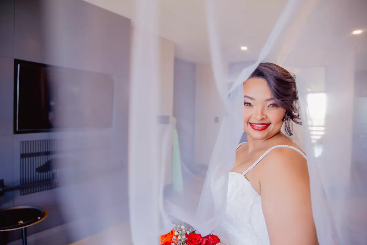 A smiling bride in a white dress and veil holding a bouquet of flowers