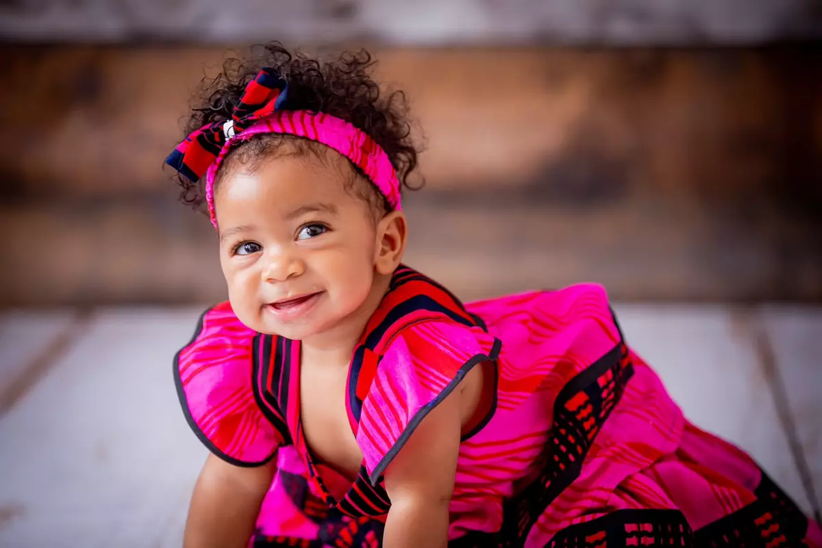 A cute baby girl with dark curly hair and a bright pink dress